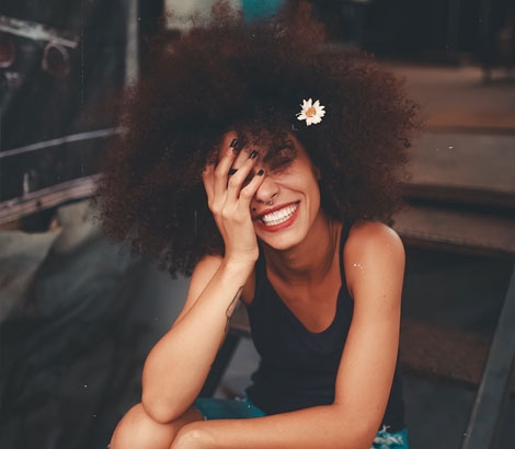 Woman with curly hair smiling while holding her face with a hand.