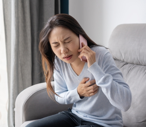 Woman clutching her chest in pain while making a phone call