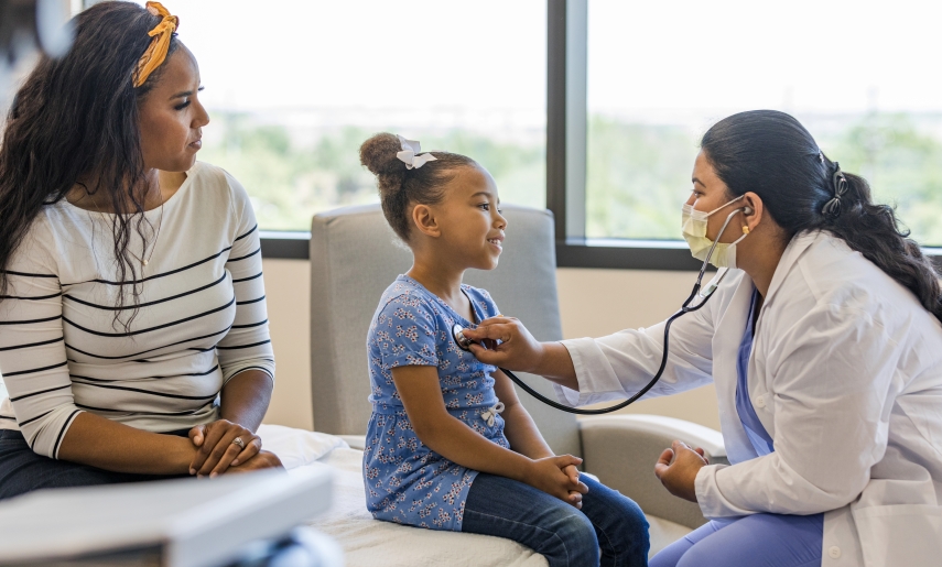 doctor examines her young patient while her mother sits close by